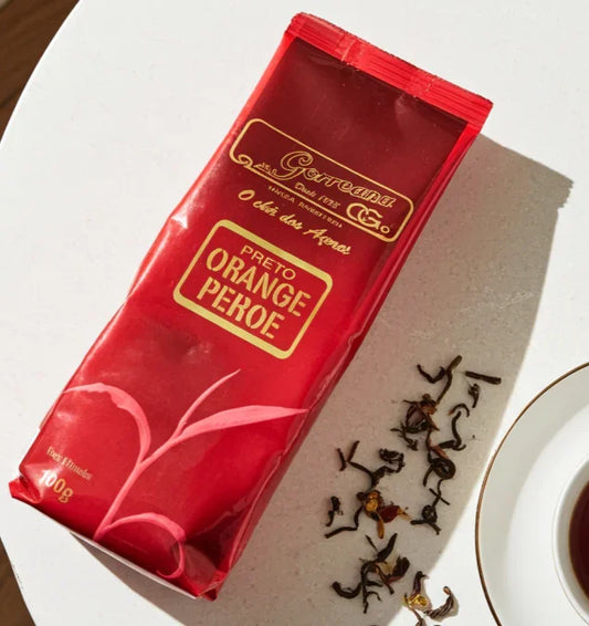 Red package of Gorreana Preto Orange Pekoe black tea with loose tea leaves and a cup of brewed tea on white surface