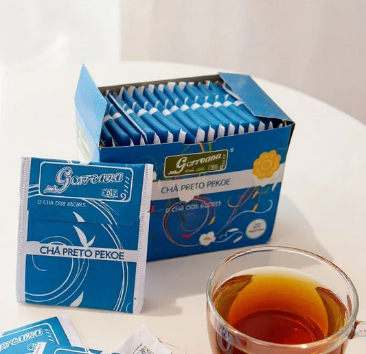 Box and packets of Garcena Chá Preto Pekoe black tea with a cup of brewed tea on white table