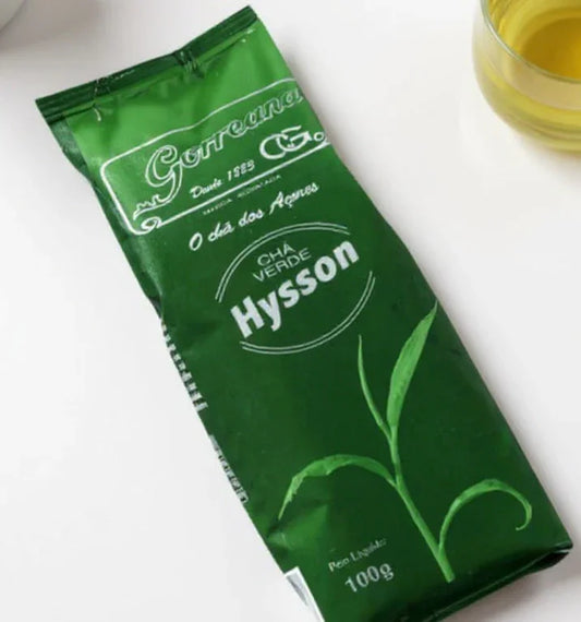 Green Hysson loose leaf tea package with a glass of brewed green tea on a white surface